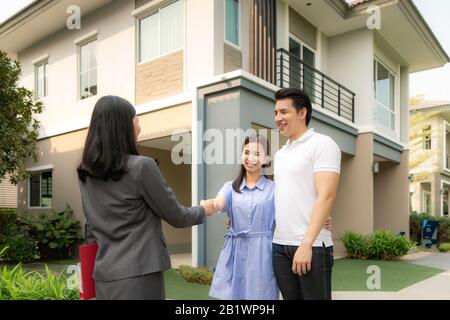 Asian felice sorriso giovane coppia stretta di mano con agente immobiliare o agente immobiliare di fronte alla loro casa dopo la firma contratto di accordo, concetto per il bene immobile Foto Stock