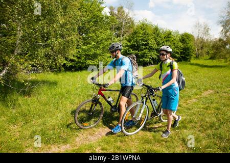 Attiva giovane coppia in bicicletta su una strada forestale in montagna in una giornata di primavera Foto Stock