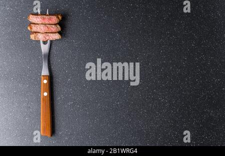 Bistecca di manzo di manzo di New york su una forchetta di carne su sfondo di pietra nera. Foto Stock