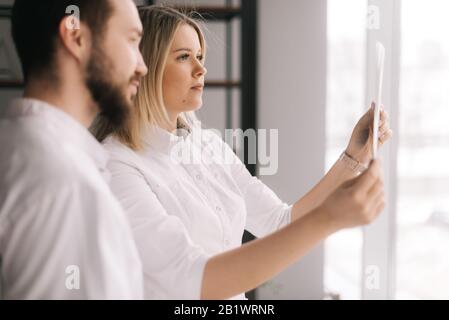 Il team medico di due giovani medici discute i raggi X del paziente nella sala riunioni Foto Stock