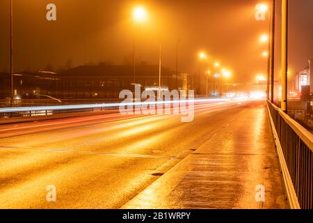 Bella luce colorata sfocata tracce di traffico notturno occupato sul ponte, luci di strada nebbia autunno tempo, città strada umida, lunga esposizione foto notturna Foto Stock