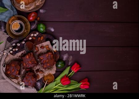 Colazione di Pasqua con caffè espresso fresco aromatico, croissant, torta brownie, uova colorate, tulipani rossi e salice. Caffè con dolci, fiori su un tavolo di legno. Vista dall'alto Foto Stock