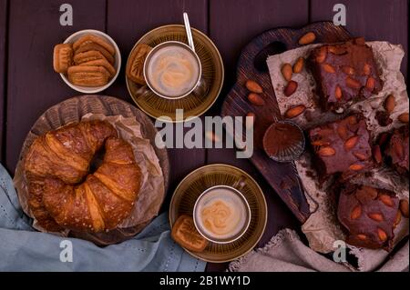 Due tazze di caffè aromatico e croissant appena sfornati, Brownie su sfondo di legno. Espresso. Vista Dall'Alto Foto Stock