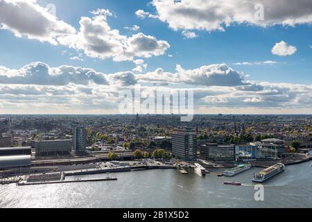 Zona portuale nel centro di Amsterdam, Paesi Bassi, vista da un alto punto di osservazione privilegiato contro un cielo blu con nuvole che guardano verso la città storica Foto Stock