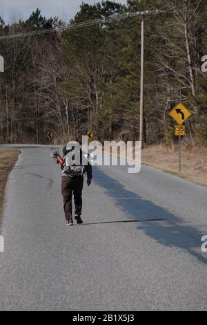 Milford, Delaware, Stati Uniti. 27th Feb, 2020. Dave WHITSON raggiunge per la sua bottiglia d'acqua mentre cammina in un headwind segnalato essere 20 miglia all'ora lungo una strada pavimentata rurale fra Milford, DE e Denton, MD il 27 febbraio 2020. Whitson, un insegnante di storia delle scuole superiori di Portland, Oregon, sta camminando per incontrare e parlare con le persone lungo il suo percorso per capire meglio e connettersi con l'America rurale. Foto Stock