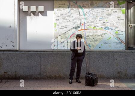 Un uomo giapponese controlla il suo smartphone di fronte a una mappa della zona di Shibuya. Piazza Hachiko, Shibuya, Tokyo, Giappone, Foto Stock