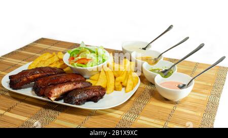 Piatto di costolette barbecue accompagnato da patatine fritte e insalata di pomodoro e lattuga su sfondo bianco Foto Stock