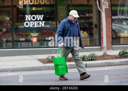 Un cliente attraversa Pike Street dopo aver effettuato acquisti presso Amazon Go Grocery il 27 febbraio 2020. Il primo supermercato cashierless di dimensioni standard della società tecnologica è stato inaugurato nel quartiere Capitol Hill di Seattle all’inizio della settimana. I clienti eseguono la scansione di un'app Amazon Go per accedere al negozio di 10.000 piedi quadrati, prendere i prodotti e andare senza effettuare il check-out. La "Just Walk Out Technology" di Amazon utilizza un sistema complesso di telecamere e sensori per tenere traccia degli acquisti già in uso nei loro piccoli negozi Amazon Go. Foto Stock