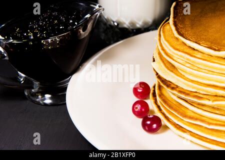 Deliziosa colazione a base di pancake appena sfornati su un piatto bianco con latte in vetro, marmellata di mirtilli e mirtilli freschi Foto Stock