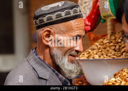 Profilo degli anziani, uyghur uomo con barba lunga e grigia. Indossa un tradizionale berretto. Minoranza musulmana di uyghur nello Xinjiang / Cina. Foto Stock
