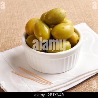 Piccola ciotola di grandi olive verdi dalla Sicilia su un tovagliolo bianco pulito piegato con stuzzicadenti in primo piano Foto Stock