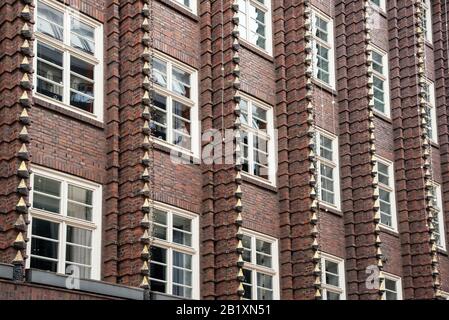 Facciata in mattoni marroni dell'edificio del palazzo con finestre e finestre verticali decorative, vista da basso angolo in pieno telaio Foto Stock