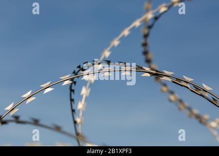 Dettaglio di / vista isolata su filo metallico/filo spinato affilato. Cielo blu sullo sfondo. Simbolo di frontiera, limitazione della migrazione, prigione. Foto Stock