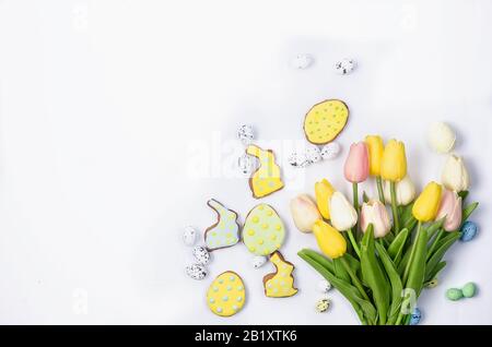 Biscotti di pan di zenzero fatti in casa di Pasqua con glassa, uova decorate e tulipani su uno sfondo bianco / concetto felice di pasqua. Spazio di copia, disposizione piatta, modello Foto Stock