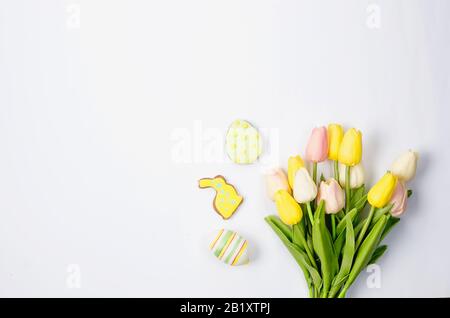 Biscotti di pan di zenzero fatti in casa di Pasqua con glassa, uova decorate e tulipani su uno sfondo bianco / concetto felice di pasqua. Spazio di copia, disposizione piatta, modello Foto Stock