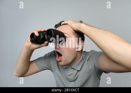 Giovane uomo scioccato guardando al futuro attraverso un binocolo su sfondo bianco Foto Stock