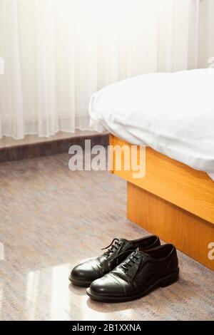 Paio di scarpe nere da uomo alla fine di un letto d'hotel Foto Stock