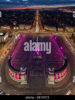 Budapest, Ungheria - veduta aerea del drone della famosa Piazza degli Eroi (Hosok tere) illuminata di notte in un colore viola e rosa unico con via Andrassy A. Foto Stock