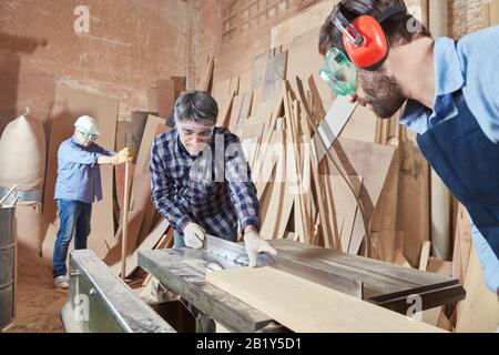 Due falegnami hanno visto legno con una sega circolare in una Falegnameria Foto Stock