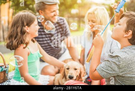 Felice famiglia facendo picnic in natura all'aperto - giovani genitori divertirsi con i bambini e il loro cane in estate ridere, giocare insieme con il sapone Foto Stock