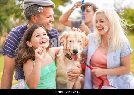 Felice famiglia facendo picnic in natura all'aperto - giovani genitori divertirsi con i bambini e il loro cane in estate ridere, giocare insieme con il sapone Foto Stock