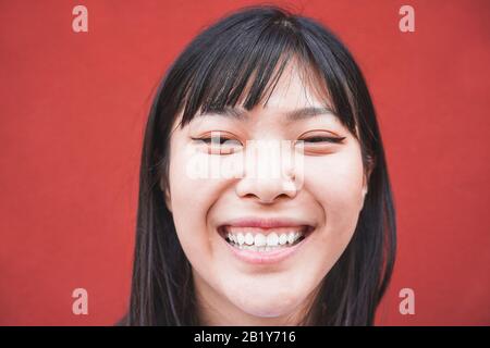 Ritratto di ragazza asiatica felice sorridente con sfondo rosso - giovane donna cinese che si diverte posando davanti alla macchina fotografica - Moda, abiti casual e Foto Stock