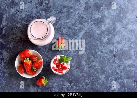 Yogurt alla fragola con frutti di bosco freschi in vetro su sfondo di pietra blu con spazio di testo libero. Concetto sano di cibo e bevande. Vista dall'alto, piatto Foto Stock