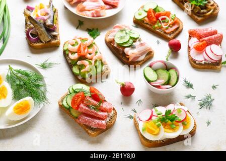 Assortimento di sandwich aperti su sfondo di pietra chiara. Diversi sandwich con carne, verdure, pesce. Gustoso spuntino sano. Foto Stock