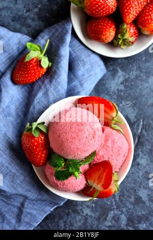 Gelato alla fragola scoop con fragole fresche in ciotola su sfondo di pietra blu. Gustoso dessert freddo estivo. Vista dall'alto, piatto Foto Stock