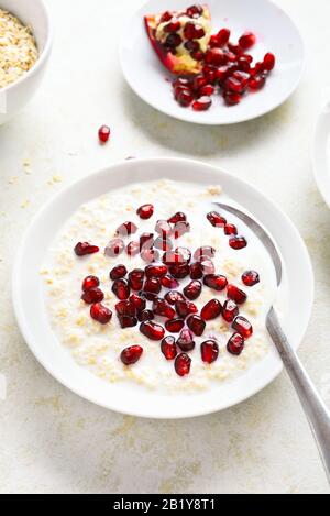 Melograno avena porridge in ciotola su sfondo di pietra chiaro. Gustoso cibo sano per la colazione o il pranzo. Foto Stock