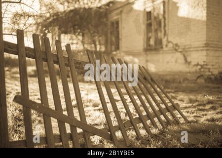 Vecchia recinzione in legno e casa di campagna in estate. Stile retrò seppia Foto Stock
