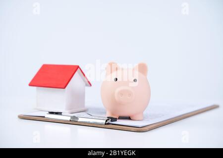 Banca piggy, modello di casa di legno bello sopra un contratto firmato su sfondo bianco, concetto di risparmio di soldi per comprare un'assicurazione domestica, primo piano, copia s. Foto Stock