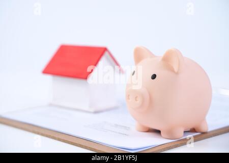 Banca piggy, modello di casa di legno bello sopra un contratto firmato su sfondo bianco, concetto di risparmio di soldi per comprare un'assicurazione domestica, primo piano, copia s. Foto Stock