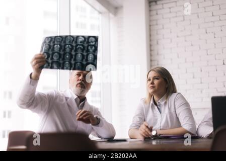 Il team di tre medici discute i raggi X del paziente nella sala di consulenza dell'ospedale Foto Stock