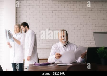 Un medico adulto esperto si siede alla sua scrivania e studia i documenti dei suoi pazienti Foto Stock