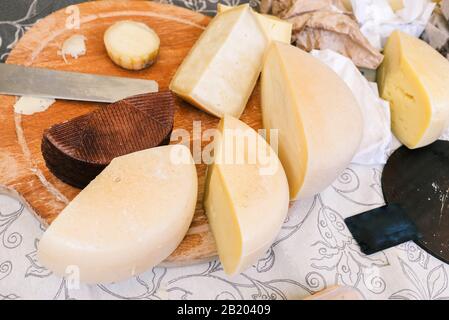 Diverse varietà di formaggio sul tavolo. Pezzi a fette di formaggio, coltello e tagliere legno Foto Stock