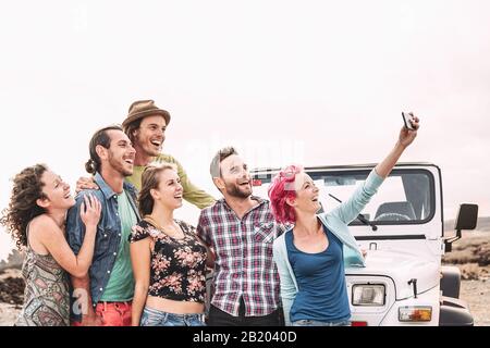 Felice amici che prendono selfie con smartphone mobile prossimo fuoristrada convertibile - Millennial giovani divertirsi facendo viaggio su strada Foto Stock