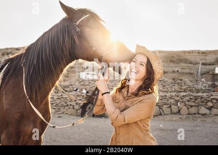 Giovane contadino che si diverte con i cavalli dentro stabile - ragazza Felice che gioca con gli animali nel ranch Corral - concetto di rapporto umano ed animale Foto Stock