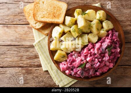 Gustosa insalata di aringhe con verdure e un piatto laterale di patate bollite da vicino in un piatto sul tavolo. Vista dall'alto orizzontale Foto Stock