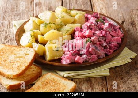 Insalata di aringa tedesca invernale con verdure e un piatto laterale di patate bollite primo piano in un piatto sul tavolo. Orizzontale Foto Stock