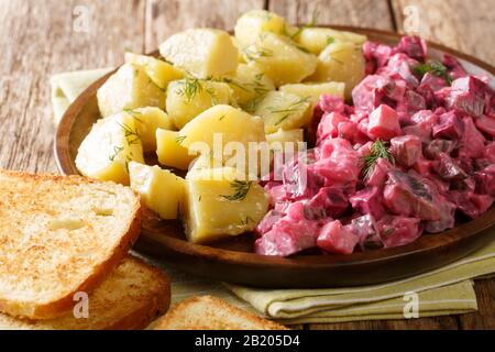 Gustosa insalata di aringhe con verdure e un piatto laterale di patate bollite da vicino in un piatto sul tavolo. Orizzontale Foto Stock