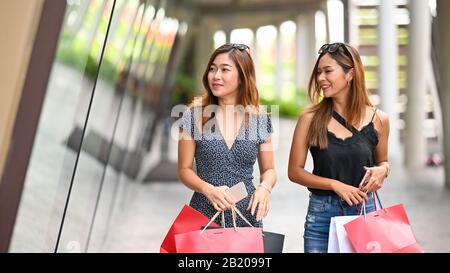 Giovani donne che camminano / parlano insieme dopo aver finito lo shopping al supermercato con bella soleggiata all'aperto come sfondo. Foto Stock