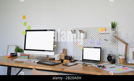 Foto del tavolo da lavoro del Graphic Designer e delle apparecchiature di progettazione grafica che lo indossano. Lo schermo bianco vuoto del computer e del computer portatile lascia spazio per Foto Stock