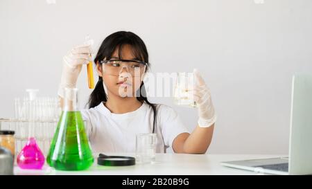 Foto di giovane adorabile ragazza in occhiali di sicurezza e guanti che tengono un matracci per la chimica, mentre fare un esperimento scienziato presso il moderno laboratorio w Foto Stock