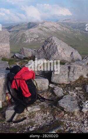 Una vista dalla cima della catena montuosa di Quinag, in Scozia, con uno zaino, un fischio e un cappotto rosso in primo piano Foto Stock