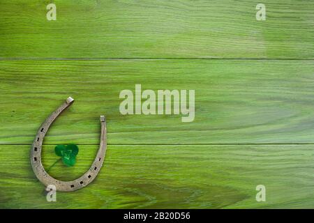 Horseshoe e trifoglio su sfondo di legno verde. Trifoglio verde della foglia. Simbolo del giorno di San Patrizio. Foto Stock