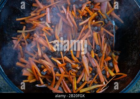 Friggere le carote affettate in olio pilaf. Le cipolle e le carote vengono fritte in una padella con olio di semi di girasole. La cottura pilaf in una grande teglia da forno su un fuoco aperto. Foto Stock