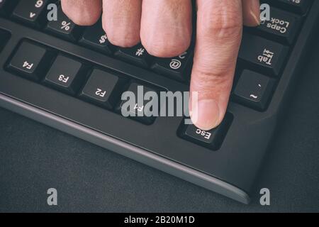 Dito della persona che preme il tasto Esc su una tastiera nera del computer. Primo piano. Foto Stock