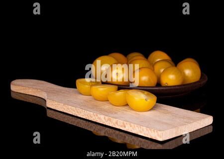 Gruppo di lotti interi quattro metà di pomodoro fresco giallo su tagliere di legno isolato su vetro nero Foto Stock