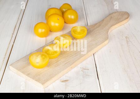 Gruppo di cinque intere quattro metà di pomodoro fresco giallo su tagliere di legno su legno bianco Foto Stock